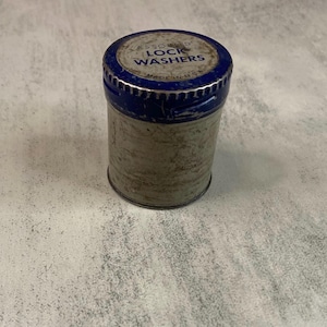 May include: A cylindrical metal container with a blue lid and the words "ASSORTED LOCK WASHERS" printed on it. The container is silver with signs of wear and tear, suggesting age. The lid has a blue rim and a silver center.
