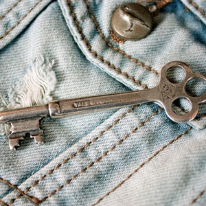 May include: A silver skeleton key with a four-pronged head, resting on a blue denim fabric background. The key has the inscription "Yale & Towne" on the shaft.