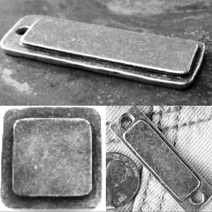 May include: Three silver metal tags with a distressed finish. The tags are rectangular and have rounded corners. The top tag is larger than the other two. The bottom two tags are smaller and have holes in the top corners.