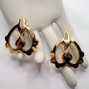 以下が含まれることがあります： ハート型のデザインのゴールドトーンのクリップ式イヤリングのペア。イヤリングは繊細で複雑なパターンをしています。