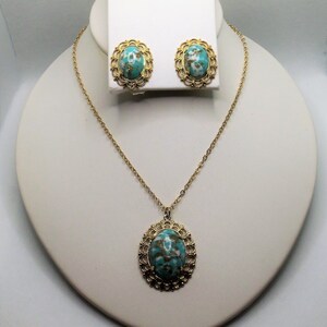 May include: A gold necklace and earrings set with a turquoise and gold oval pendant and matching earrings. The pendant and earrings have a delicate filigree design.