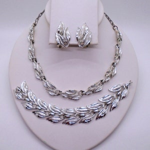 Op de afbeelding: Een zilverkleurige set met een ketting, armband en oorbellen met een bladontwerp. De sieraden worden getoond op een witte mannequinbuste.
