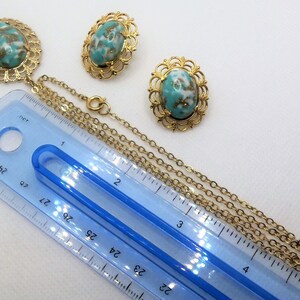 May include: A gold tone necklace with a turquoise and gold oval pendant and matching earrings. The necklace is 22 inches long and has a chain link design. The pendant and earrings have a filigree design.