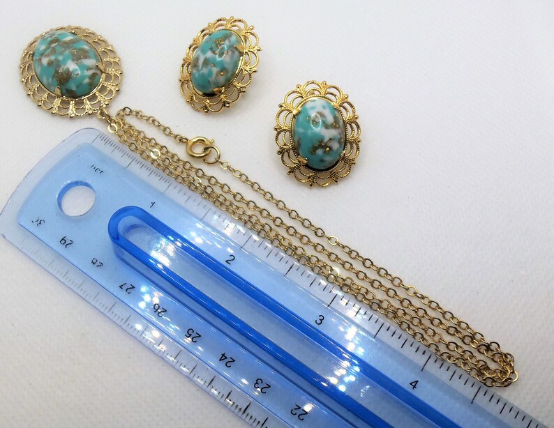 May include: A gold tone necklace with a turquoise and gold oval pendant and matching earrings. The necklace is 22 inches long and has a chain link design. The pendant and earrings have a filigree design.