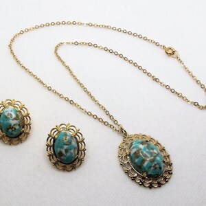 May include: A gold chain necklace with a turquoise and white oval pendant and matching earrings. The pendant and earrings have a gold filigree design.