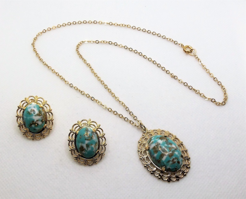 May include: A gold chain necklace with a turquoise and white oval pendant and matching earrings. The pendant and earrings have a gold filigree design.