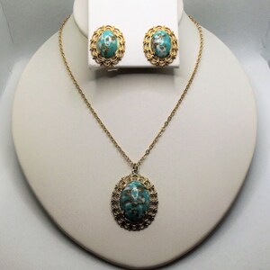 May include: A gold necklace and earrings set with a turquoise and gold oval pendant and matching earrings. The pendant and earrings have a delicate filigree design.