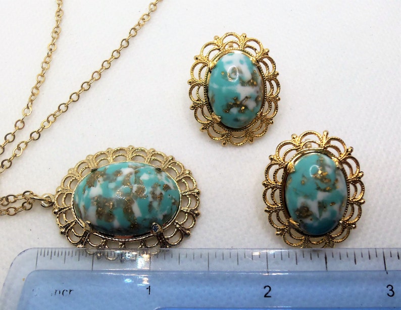 May include: A gold chain necklace with a turquoise and gold oval pendant. The pendant has a delicate filigree design. Matching earrings with the same design are also included.