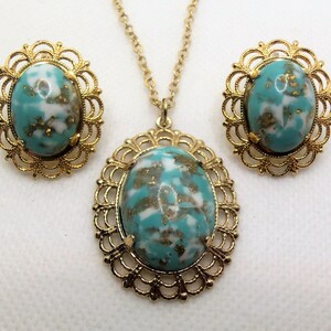 May include: A gold tone necklace and earrings set with turquoise blue and white oval stones in a filigree setting.
