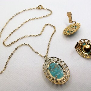 May include: A gold chain necklace with a turquoise oval pendant set in a filigree frame. Matching clip-on earrings with turquoise stones in filigree frames.