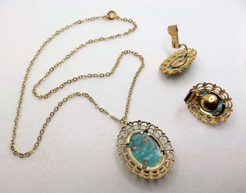 May include: A gold chain necklace with a turquoise oval pendant set in a filigree frame. Matching clip-on earrings with turquoise stones in filigree frames.