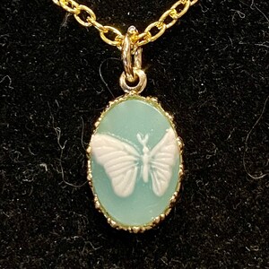 May include: A gold chain necklace with a light blue oval pendant featuring a white butterfly design.