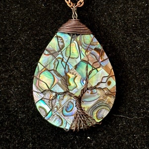 May include: A copper wire wrapped pendant featuring a tree of life design with iridescent abalone shell inlay. The pendant is attached to a copper chain.
