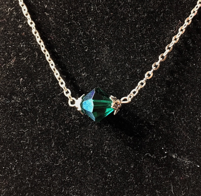 Op de afbeelding: Een zilveren ketting met een donkergroene gefacetteerde kristallen hanger.