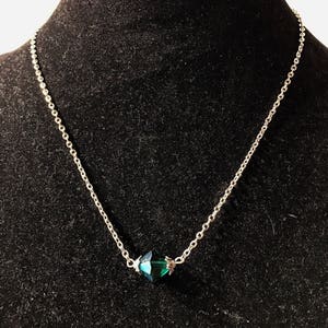 Op de afbeelding: Een zilveren ketting met een donkergroene gefacetteerde kristallen hanger.
