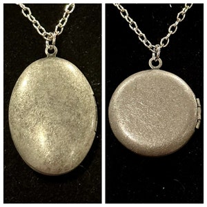 May include: A silver locket necklace with a round pendant. The locket has a textured surface and a hinged opening.