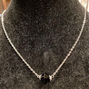 Op de afbeelding: Een zilveren ketting met een zwarte gefacetteerde edelsteen hanger.