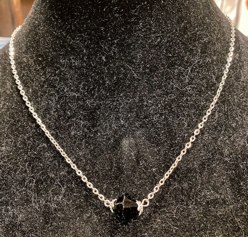 Op de afbeelding: Een zilveren ketting met een zwarte gefacetteerde edelsteen hanger.