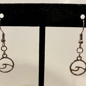 以下が含まれることがあります： 波のカットアウトが施された円形のデザインのシルバー製ドロップイヤリング