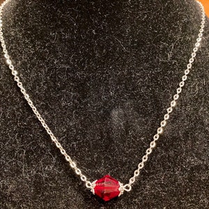 Op de afbeelding: Een zilveren ketting met een enkele, gefacetteerde, donkerrode edelsteen hanger.