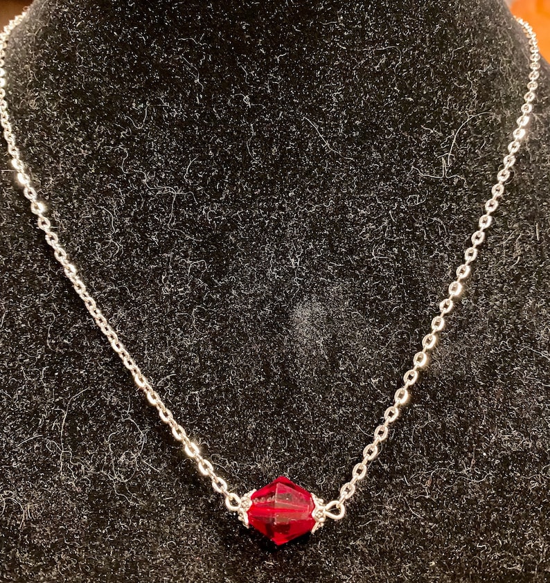 Op de afbeelding: Een zilveren ketting met een enkele, gefacetteerde, donkerrode edelsteen hanger.