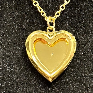 Op de afbeelding: Een gouden ketting met een hartvormige hanger. De hanger is open en de binnenkant is zichtbaar.