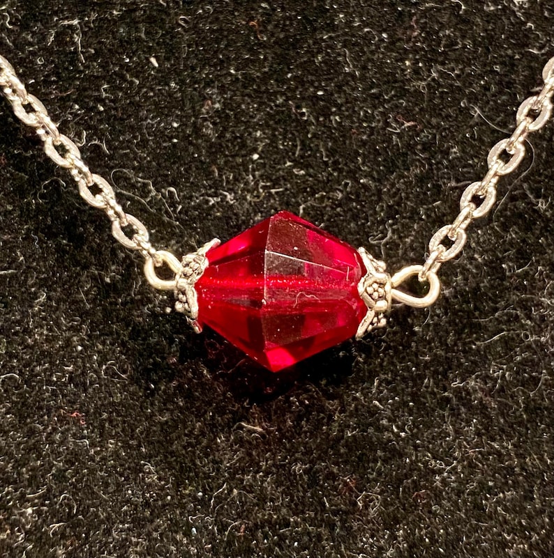 Op de afbeelding: Een zilveren ketting met een enkele, gefacetteerde, rode edelsteen hanger.