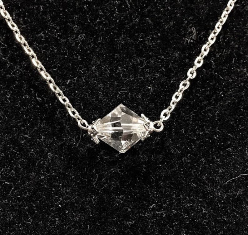 Op de afbeelding: Een zilveren ketting met een heldere kristallen hanger.