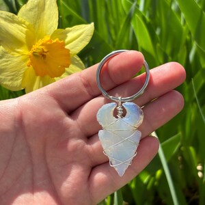 May include: A white iridescent arrowhead wrapped in silver wire, attached to a silver key ring.