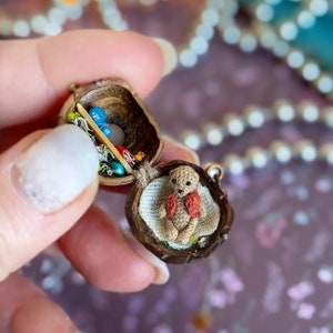 Tiny house in a walnut shell with a miniature teddy bear crocheted inside. Opening pendant