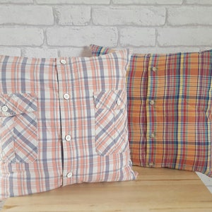 May include: Two decorative pillows made from repurposed plaid shirts. The pillow on the left is a light pink and blue plaid, and the pillow on the right is a bright orange, yellow, and blue plaid.