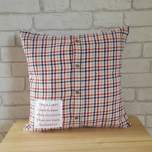May include: A red, blue, and beige plaid pillow with a white fabric patch sewn on the front. The patch has red text that reads "This is a shirt I used to wear. When you hold it know I am there. Love Dad xx".