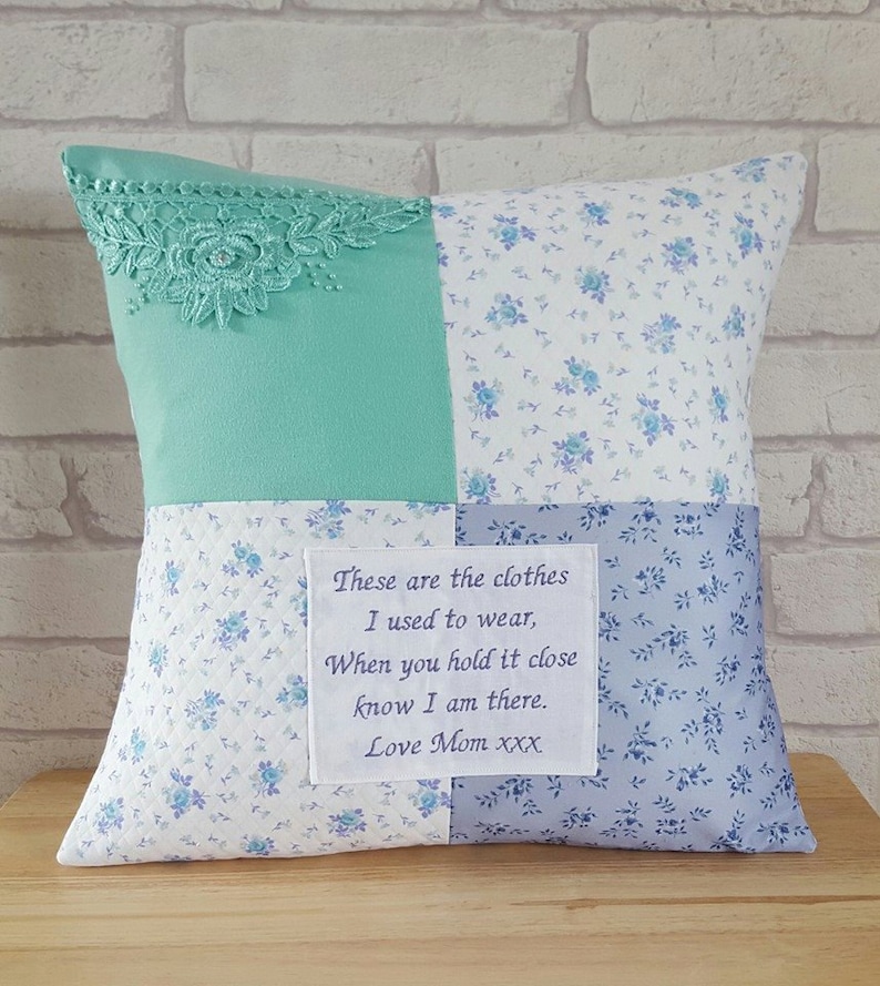 May include: A square patchwork pillow with a light blue floral pattern on three sides. The fourth side is a light green fabric with a white lace trim. A white fabric label with a message is sewn onto the pillow: "These are the clothes I used to wear, When you hold it close know I am there. Love Mom xxx".