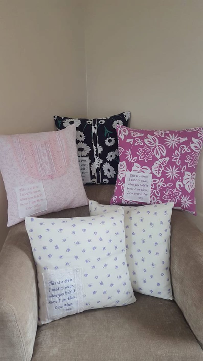 May include: Four decorative throw pillows with floral patterns and embroidered messages. The pillows are arranged on a light brown armchair. The messages on the pillows read: "This is a dress I used to wear, when you hold it know I am there. Love Mum", "This is a dress I used to wear, when you hold it know I am there. Love Mum", "This is a dress I used to wear, when you hold it know I am there. Love your sister", and "This is a dress I used to wear, when you hold it know I am there. Love Mum".