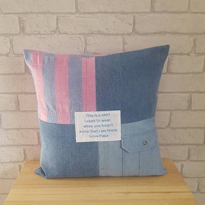 May include: A blue and pink striped pillow with a patch of denim fabric. The patch has a white label with the text "This is a shirt I used to wear. When you hold it know that I am there. Love Papa."