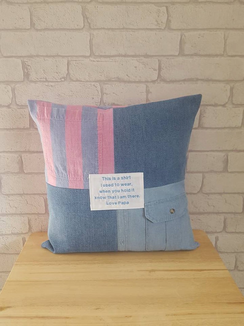 May include: A blue and pink striped pillow with a patch of denim fabric. The patch has a white label with the text "This is a shirt I used to wear. When you hold it know that I am there. Love Papa."