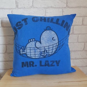 May include: Blue pillow with a white graphic of a cartoon character in a hammock. The text "Just Chillin' Mr. Lazy" is printed on the pillow.