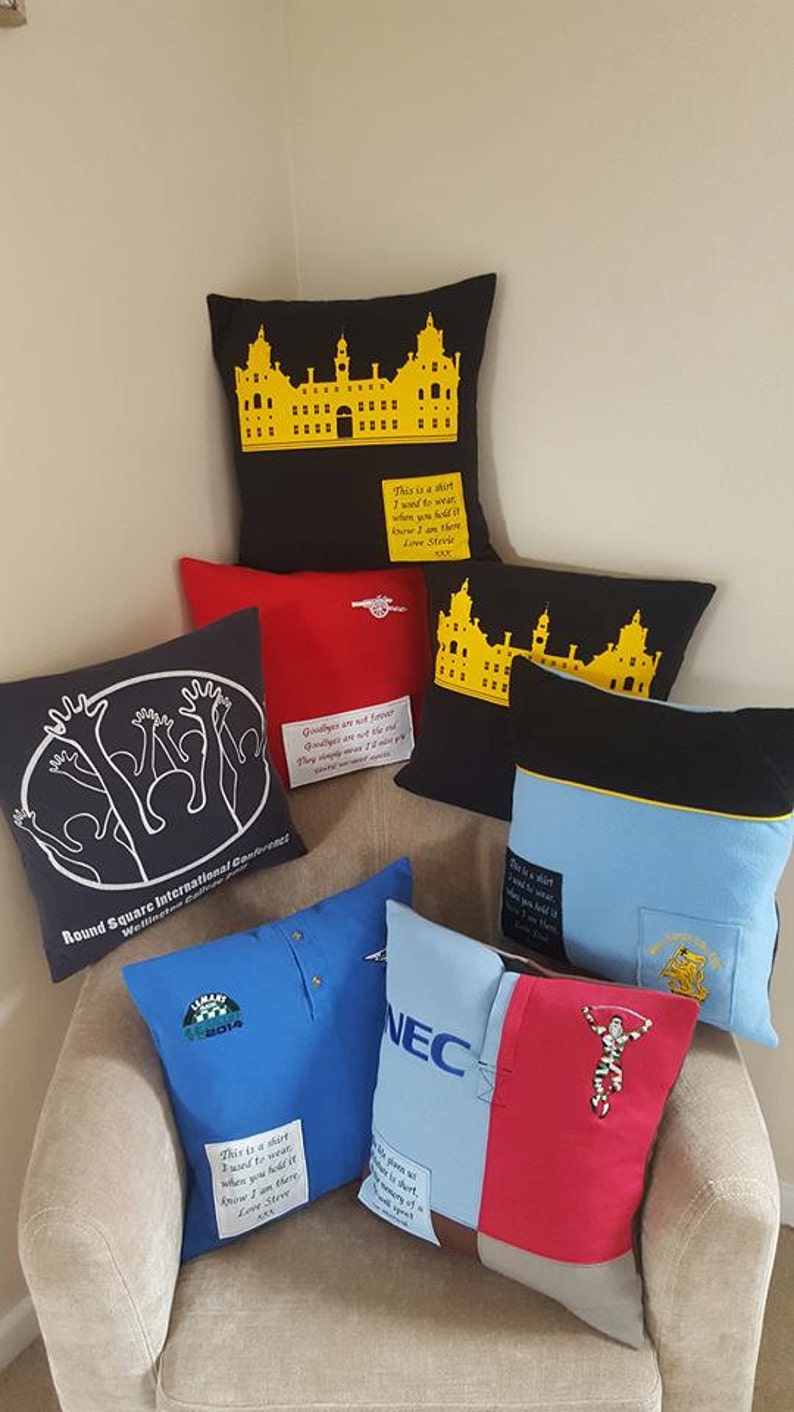 May include: A collection of decorative throw pillows with various designs and colors. The pillows feature different fabrics, including blue, red, black, and white. Some pillows have embroidered text, such as "This is a shirt I want to wear. When you hold it know I am there. Love Steve."