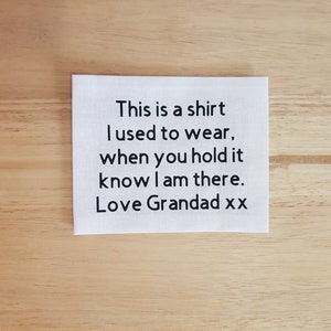 May include: White fabric square with black text that reads "This is a shirt I used to wear, when you hold it know I am there. Love Grandad xx"