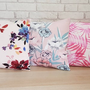 May include: Three decorative throw pillows with floral and leaf patterns. The pillows are pink, white, and blue with watercolor-style designs.