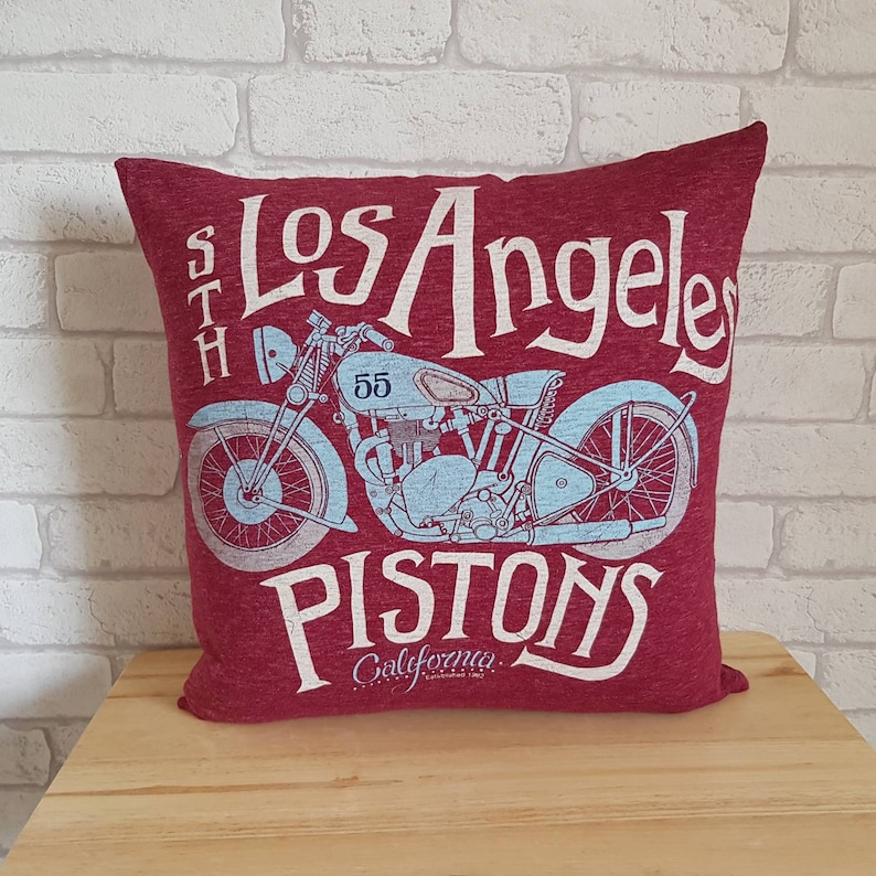 May include: Red throw pillow with a vintage motorcycle graphic and the text "Los Angeles Pistons California Established 1962".