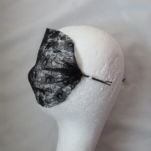 May include: Black lace mask with a floral pattern, attached to a white mannequin head with a bobby pin.