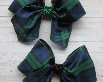 May include: Two large plaid bows with green and blue plaid patterns and black centers. The bows are made of satin ribbon and have a sparkly center.