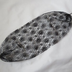 May include: Black lace hair net with a floral pattern. The net is gathered at the top and has two strings attached to the sides.