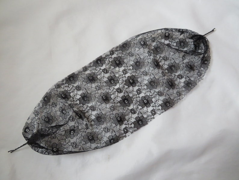 May include: Black lace hair net with a floral pattern. The net is gathered at the top and has two strings attached to the sides.