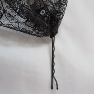 May include: A black lace fabric with a black bobby pin attached to the bottom.