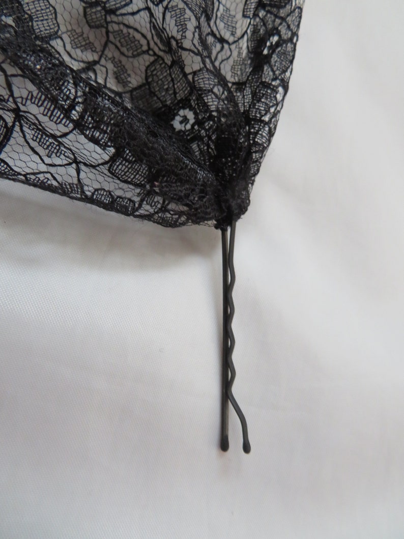 May include: A black lace fabric with a black bobby pin attached to the bottom.