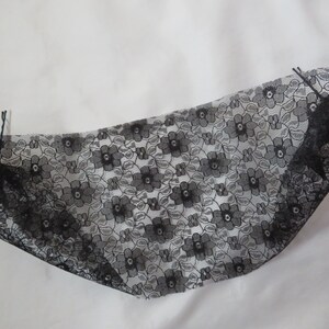 May include: Black lace fabric with a floral pattern. The fabric is folded in half and has two black hair clips attached to it.