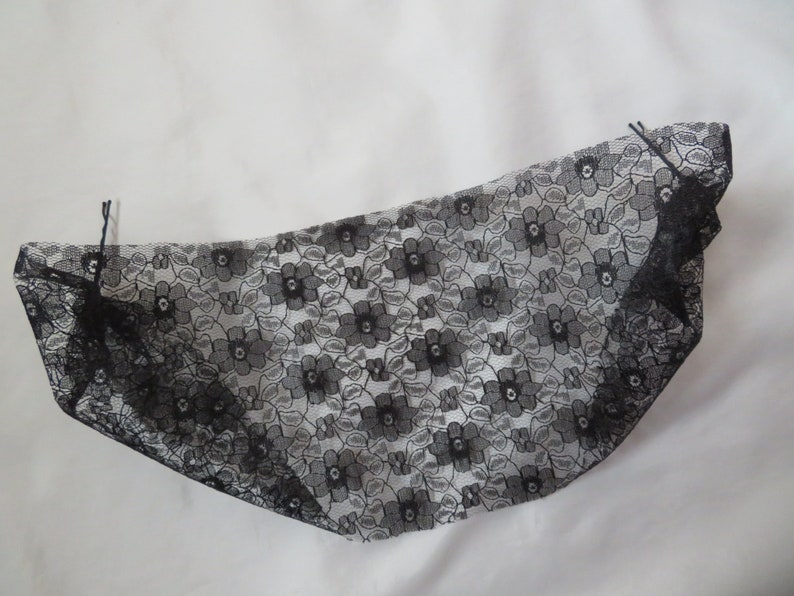 May include: Black lace fabric with a floral pattern. The fabric is folded in half and has two black hair clips attached to it.