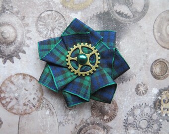 May include: A green and blue plaid fabric flower brooch with a gold gear and a green pearl in the center.